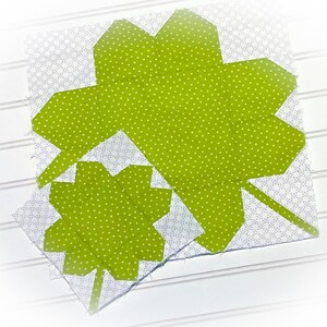 May include: Two green fabric shamrocks with white polka dots, one larger than the other, are sewn together on a white background.