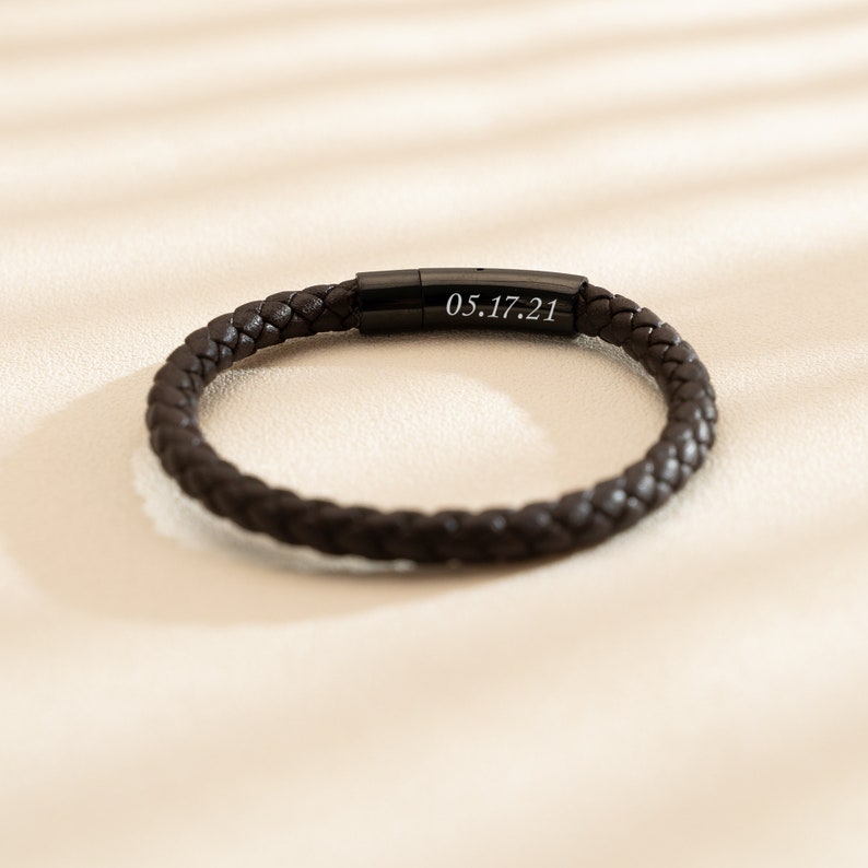 May include: A black leather bracelet with a black metal clasp engraved with the date "05.17.21".