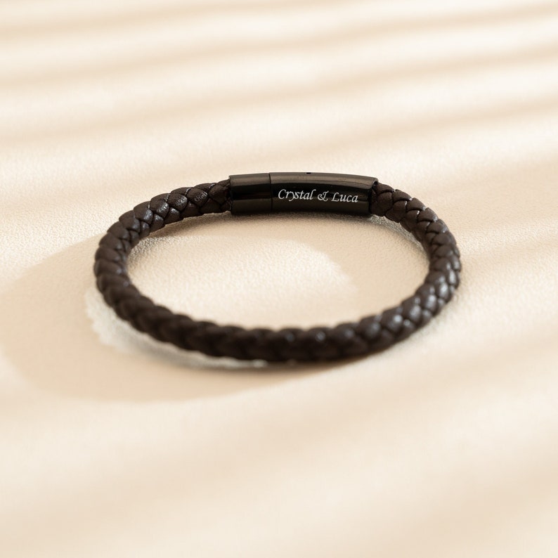 May include: A brown leather bracelet with a black metal clasp engraved with "Crystal & Luca".