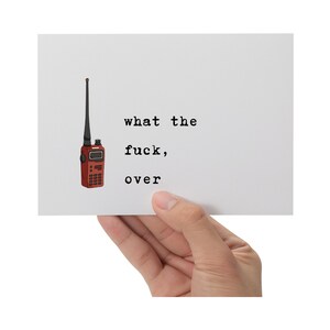 Pu&ograve; includere: Una carta bianca tenuta in mano, con un'illustrazione di walkie-talkie rosso e il testo "what the fuck, over" in nero. Il walkie-talkie ha un'antenna nera e un piccolo schermo.
