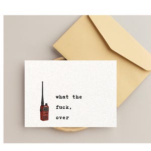 Pu&ograve; includere: Un biglietto di auguri bianco con la scritta "what the fuck, over" e un'illustrazione di walkie-talkie rosso. Una busta beige &egrave; dietro il biglietto. Il biglietto &egrave; su una superficie beige chiaro.