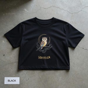 Op de afbeelding: Zwart T-shirt met een uil-afbeelding. Het ontwerp toont een bruine en witte uil op een tak, omlijst door een halve maan. Het woord "SOVEREIGN" staat onder de uil gedrukt. Het shirt is gelabeld "BLACK".