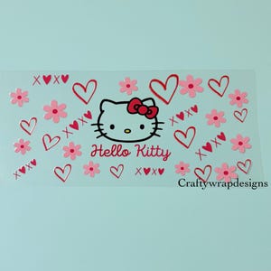 May include: A clear rectangular sticker featuring a Hello Kitty design. The design includes the Hello Kitty face, hearts, flowers, and the text "Hello Kitty" in pink. The sticker also has the text "xoxo" and "Craftywrapdesigns".