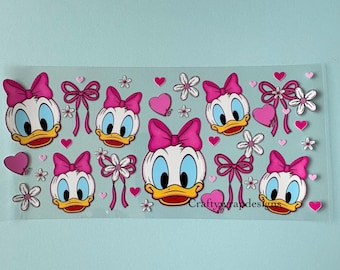 Op de afbeelding: Transparante sticker met Daisy Duck's gezicht met een roze strik, omringd door roze strikken, harten en bloemen. De sticker heeft de tekst "Craftywrapdesigns". De achtergrond is lichtblauw.