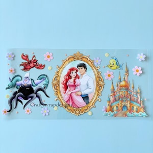 May include: A clear sticker featuring characters from The Little Mermaid. The design includes Ariel and Prince Eric in a gold frame, Ursula, Sebastian, Flounder, and a castle. The sticker is decorated with pink and purple flowers, and the text "Craftywrapdesigns" is visible.