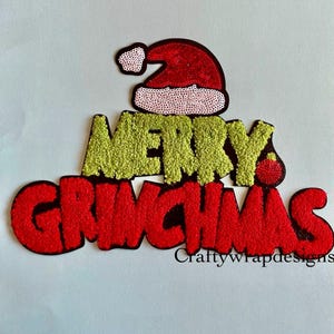 May include: A festive applique with the words "MERRY GRINCHMAS" in red and green, topped with a Santa hat. The text has a textured, glittery appearance, perfect for holiday crafts and decorations.