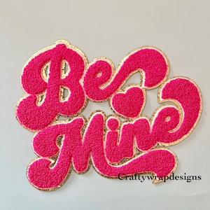 May include: Pink and gold "Be Mine" iron-on patch with a fuzzy texture.