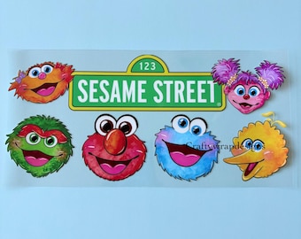 May include: A sheet of Sesame Street character stickers. The stickers include Elmo, Cookie Monster, Big Bird, and others. The Sesame Street sign is in the center. The background is a light blue.