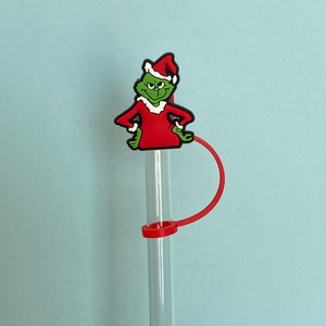 K&ouml;nnte beinhalten: Ein gr&uuml;ner und roter Grinch-Charakter-Strohhalm-Topper mit einem roten Strohhalm. Der Grinch tr&auml;gt eine Weihnachtsmannm&uuml;tze und einen roten Anzug.