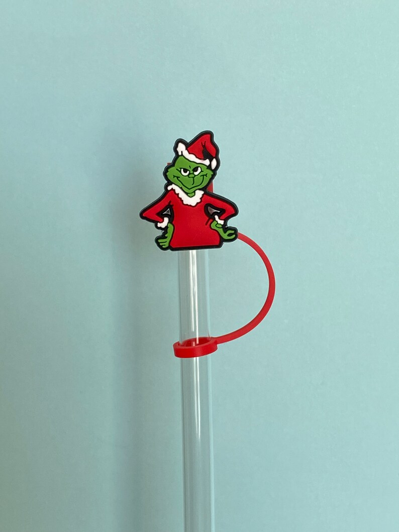 K&ouml;nnte beinhalten: Ein gr&uuml;ner und roter Grinch-Charakter-Strohhalm-Topper mit einem roten Strohhalm. Der Grinch tr&auml;gt eine Weihnachtsmannm&uuml;tze und einen roten Anzug.