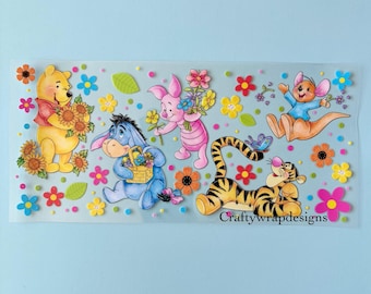 Op de afbeelding: Een doorzichtige sticker met Winnie de Poeh en vrienden. Poeh houdt zonnebloemen vast, Knorretje draagt bloemen, Iejoor heeft een mand met bloemen, Tijger ligt en Kanga springt. Kleurrijke bloemen en de tekst "Craftywrapdesigns" zijn ook inbegrepen.