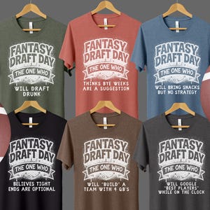 May include: A collection of six short-sleeved t-shirts in various colors, each featuring the text "FANTASY DRAFT DAY" and a humorous tagline. The shirts are displayed with two footballs. The taglines include phrases like "Will Draft Drunk" and "Believes Tight Ends Are Optional."