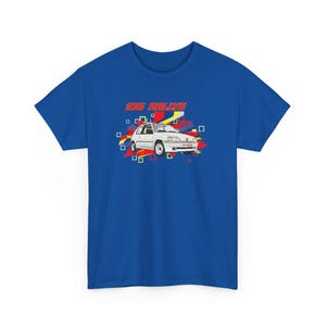 May include: Royal blue t-shirt featuring a graphic of a white car with the text "106 Rallye" in red and yellow. The car graphic is surrounded by red, yellow, and white geometric shapes. A classic car design.