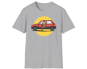 May include: A grey t-shirt with a cartoon image of a red car and a person inside, set against a yellow circle. The car door is open. The design is in the centre of the shirt.