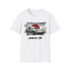 May include: White t-shirt featuring a graphic of a light green sports car with pop-up headlights, set against a red sun and gray background. The text "MX-5" is printed below the car in black. The shirt is a classic crew neck.