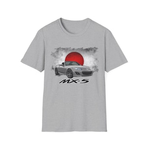 May include: A light gray t-shirt featuring a graphic of a silver MX-5 convertible car in front of a red sun and white clouds. The text "MX-5" is below the car in white.