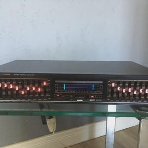 May include: Black Fisher Stereo Graphic Equalizer with illuminated controls. The unit has multiple sliders and a central display. The text "Fisher Standard - STEREO" is visible on the top left.