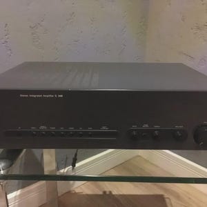 Könnte beinhalten: Schwarzer NAD Stereo-Vollverstärker C 340. Die Frontplatte hat verschiedene Tasten und Knöpfe für Lautstärke, Balance und Eingangswahl. Der Text "NAD Stereo Integrated Amplifier C 340" ist auf der Vorderseite aufgedruckt.