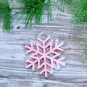 K&ouml;nnte beinhalten: Rosa glitzernder Schneeflocken-Anh&auml;nger mit transparentem Hintergrund. Der Anh&auml;nger hat oben ein Loch zum Aufh&auml;ngen.