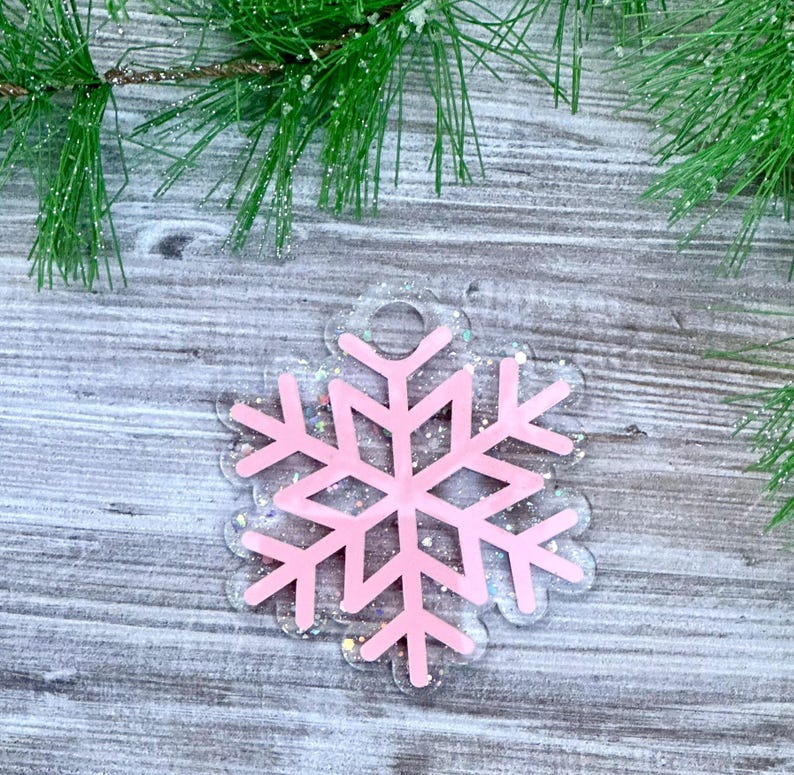 K&ouml;nnte beinhalten: Rosa glitzernder Schneeflocken-Anh&auml;nger mit transparentem Hintergrund. Der Anh&auml;nger hat oben ein Loch zum Aufh&auml;ngen.