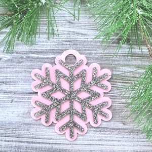 K&ouml;nnte beinhalten: Rosa Schneeflocken-Anh&auml;nger mit silbernem Glitzer. Der Anh&auml;nger hat oben ein Loch zum Aufh&auml;ngen.