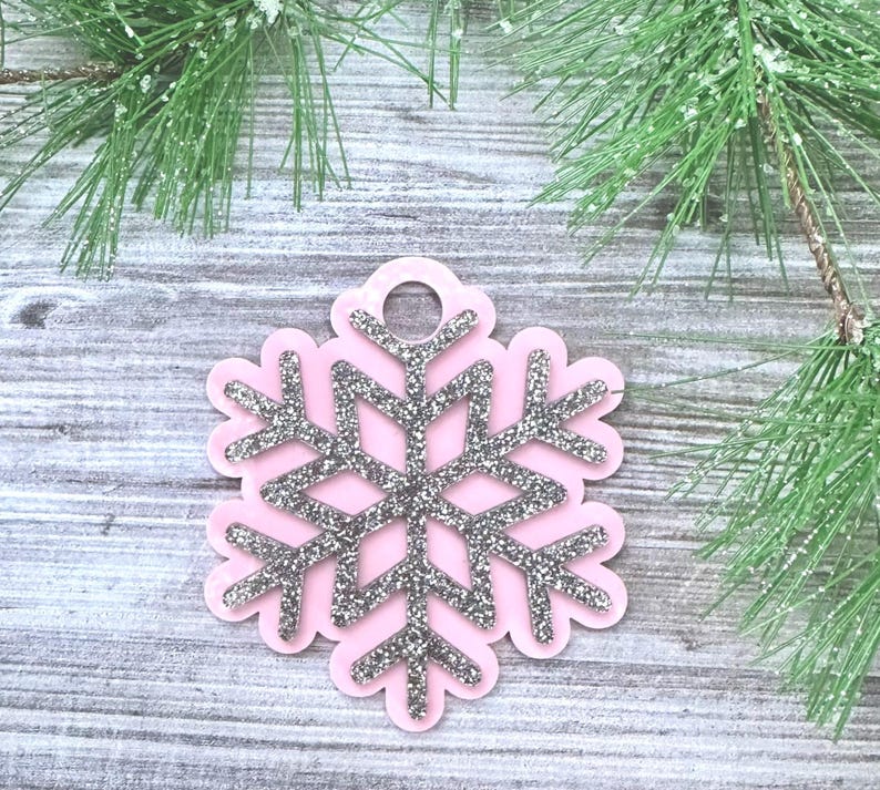 K&ouml;nnte beinhalten: Rosa Schneeflocken-Anh&auml;nger mit silbernem Glitzer. Der Anh&auml;nger hat oben ein Loch zum Aufh&auml;ngen.