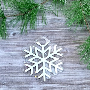 K&ouml;nnte beinhalten: Wei&szlig;er Schneeflocken-Anh&auml;nger mit glitzerndem, irisierendem Finish. Der Anh&auml;nger hat oben ein Loch zum Aufh&auml;ngen.