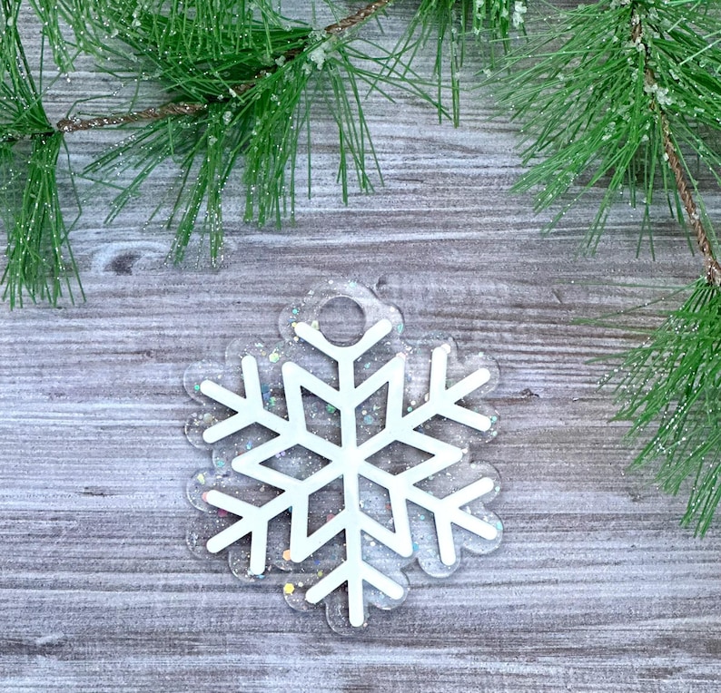 K&ouml;nnte beinhalten: Wei&szlig;er Schneeflocken-Anh&auml;nger mit glitzerndem, irisierendem Finish. Der Anh&auml;nger hat oben ein Loch zum Aufh&auml;ngen.