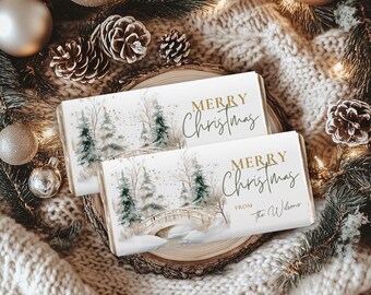 May include: Two white chocolate bar wrappers with a winter scene of trees and a bridge, with the words "MERRY Christmas" in gold script. The bars are on a wooden slice, surrounded by pine needles, ornaments, and pine cones.