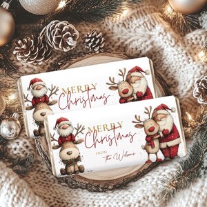 Könnte beinhalten: Zwei weiße, rechteckige Geschenkboxen zum Thema Weihnachten mit Illustrationen von Weihnachtsmann und Rentieren. Die Boxen tragen den Text "MERRY Christmas" in goldener Schrift. Eine Box hat den zusätzlichen Text "from the Wilsons".