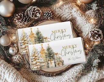 May include: Two rectangular Christmas-themed gift tags with the words "MERRY CHRISTMAS" in gold script. The tags feature watercolor illustrations of Christmas trees and wrapped gifts. The tags are placed on a wooden slice, surrounded by pine needles, ornaments, and pine cones.