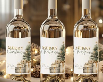 May include: Three clear glass wine bottles with beige caps and labels that read "Merry Christmas." The labels feature a Christmas tree and wrapped gifts. The bottles are on a white surface with Christmas lights in the background.