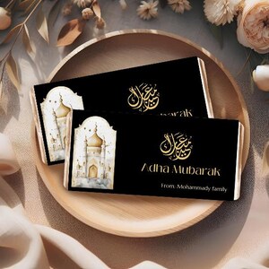 Peut inclure: Deux cartes rectangulaires noires avec calligraphie dor&eacute;e et les mots "Adha Mubarak" sont pr&eacute;sent&eacute;es sur un plateau en bois. Une carte pr&eacute;sente une illustration &agrave; l'aquarelle d'une mosqu&eacute;e. Les cartes sont entour&eacute;es de d&eacute;corations florales.