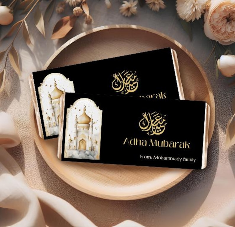 Peut inclure: Deux cartes rectangulaires noires avec calligraphie dor&eacute;e et les mots "Adha Mubarak" sont pr&eacute;sent&eacute;es sur un plateau en bois. Une carte pr&eacute;sente une illustration &agrave; l'aquarelle d'une mosqu&eacute;e. Les cartes sont entour&eacute;es de d&eacute;corations florales.