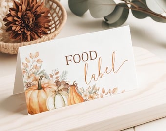 May include: A folded food label with the words "FOOD label" in brown script. The label features watercolor illustrations of pumpkins and fall foliage in shades of orange, white, and brown. The label is on a light wooden surface.