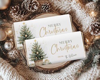 May include: Two white chocolate bar wrappers with gold text that reads "MERRY Christmas" and a watercolor Christmas tree design. One wrapper also says "FROM The Wilones". The bars are on a wooden slice with pine cones and ornaments.