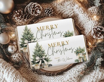 May include: Two rectangular Christmas-themed gift boxes with the text "MERRY CHRISTMAS" in gold script. Each box features a watercolor Christmas tree, gifts, and a bow. The boxes are on a wooden slice, surrounded by pinecones, ornaments, and greenery.