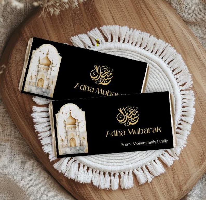 Peut inclure: Deux emballages de barres chocolat&eacute;es noirs avec une calligraphie dor&eacute;e et les mots "Adha Mubarak". L'un des emballages pr&eacute;sente une image aquarelle d'une mosqu&eacute;e. L'emballage du bas comprend "From: Mohammady family."