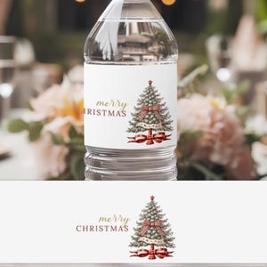 Puede incluir: Una botella de agua transparente con una etiqueta blanca con un diseño de árbol de Navidad. La etiqueta incluye las palabras "merry CHRISTMAS" en letras doradas. El árbol está decorado con un lazo a cuadros rojo y blanco y cinta roja.