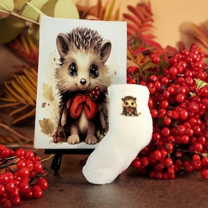May include: A white sock with a small embroidered hedgehog design. The sock is next to a framed illustration of a hedgehog with a red bow.