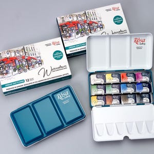 May include: A set of 12 watercolour paints in a teal and white metal tin. The tin has a removable tray with 12 individual paint pans. The paint pans are labelled with the colour name and number. The tin also has a lid with a built-in palette. The lid features a colourful illustration of a street scene with people and buildings. The text on the tin reads "Rosa Gallery Watercolours Urban Sketching 12.0ml Produced in Ukraine Developed in collaboration with professional artists."