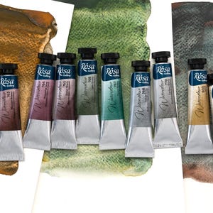 Op de afbeelding: Een collectie van tien Rosa Gallery aquarelverftubes met zwarte doppen, elk voorzien van een kleurnaam en nummer, gerangschikt tegen drie verschillende geschilderde aquarelstalen in tinten bruin, groen en grijs.