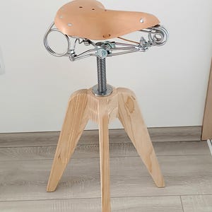 May include: A wooden tripod stool with a brown leather bicycle seat.