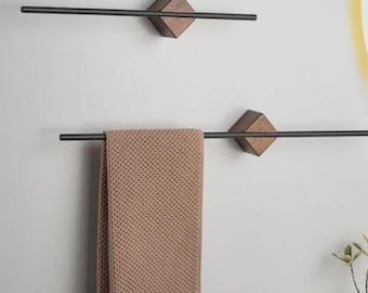 May include: Two modern towel racks with a minimalist design. Each rack features a dark metal bar attached to a wooden diamond-shaped mount. A tan towel hangs from the lower rack. The racks are mounted on a white wall.