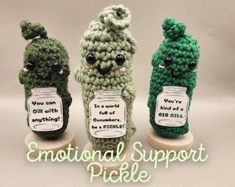May include: Three crocheted pickle plush toys, each holding a jar with a different saying. The first pickle says "You can Dill with anything!" The second pickle says "In a world full of Cucumbers, be a PICKLE!" The third pickle says "You're kind of a BIG DILL!" The pickles are green and have cute faces. The text "Emotional Support Pickle" is written below the pickles.