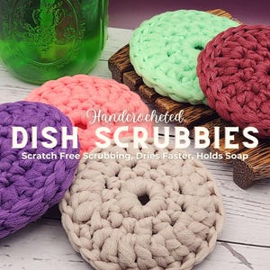 Pode incluir: Cinco esfregões de pratos feitos à mão em crochê de várias cores, incluindo roxo, rosa, verde, bege e vermelho. Os esfregões são exibidos em uma superfície de madeira com o texto "Handcrocheted DISH SCRUBBIES Scratch Free Scrubbing, Dries Faster, Holds Soap".
