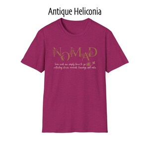 May include: A short-sleeved, magenta t-shirt with the word "NOMAD" in gold script. Below the word is the text "Some souls are simply born to go collecting stories, moments, learnings and miles."