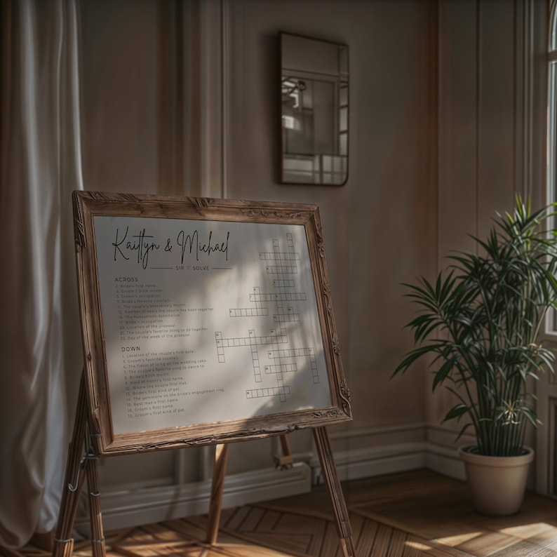 May include: A wooden easel displaying a white crossword puzzle. The puzzle is titled "Kaitlyn & Michael" and features wedding-themed clues. The easel is situated in a room with a mirror and a potted plant.