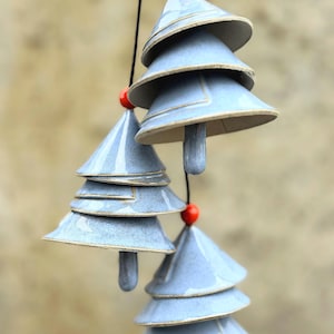 Könnte beinhalten: Hängende Keramik-Windspiele in Form stilisierter Weihnachtsbäume. Jeder Baum besteht aus geschichteten, hellblauen, kegelförmigen Abschnitten mit braunem Rand. Auf jedem Baum und zwischen den Abschnitten befindet sich eine kleine rote Perle.