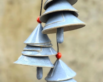 May include: Hanging ceramic wind chimes in the shape of stylized Christmas trees. Each tree is composed of layered, light blue, cone-shaped sections with a brown rim. A small red bead sits atop each tree and between the sections.